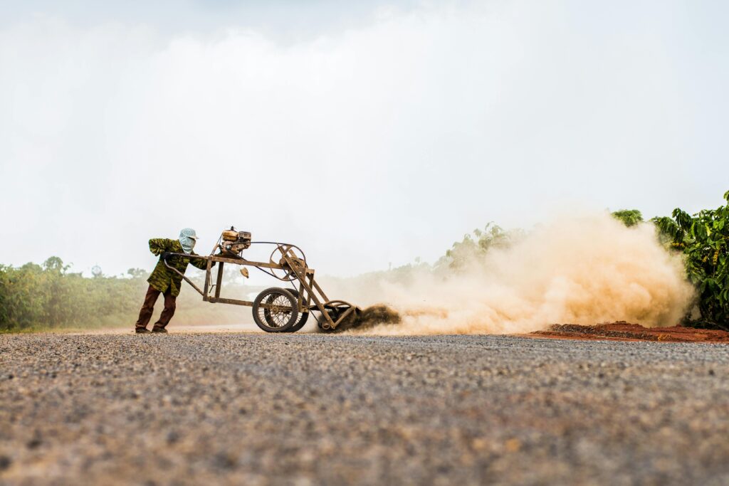 Man using machinery to grade a dusty road in a rural outdoor setting.